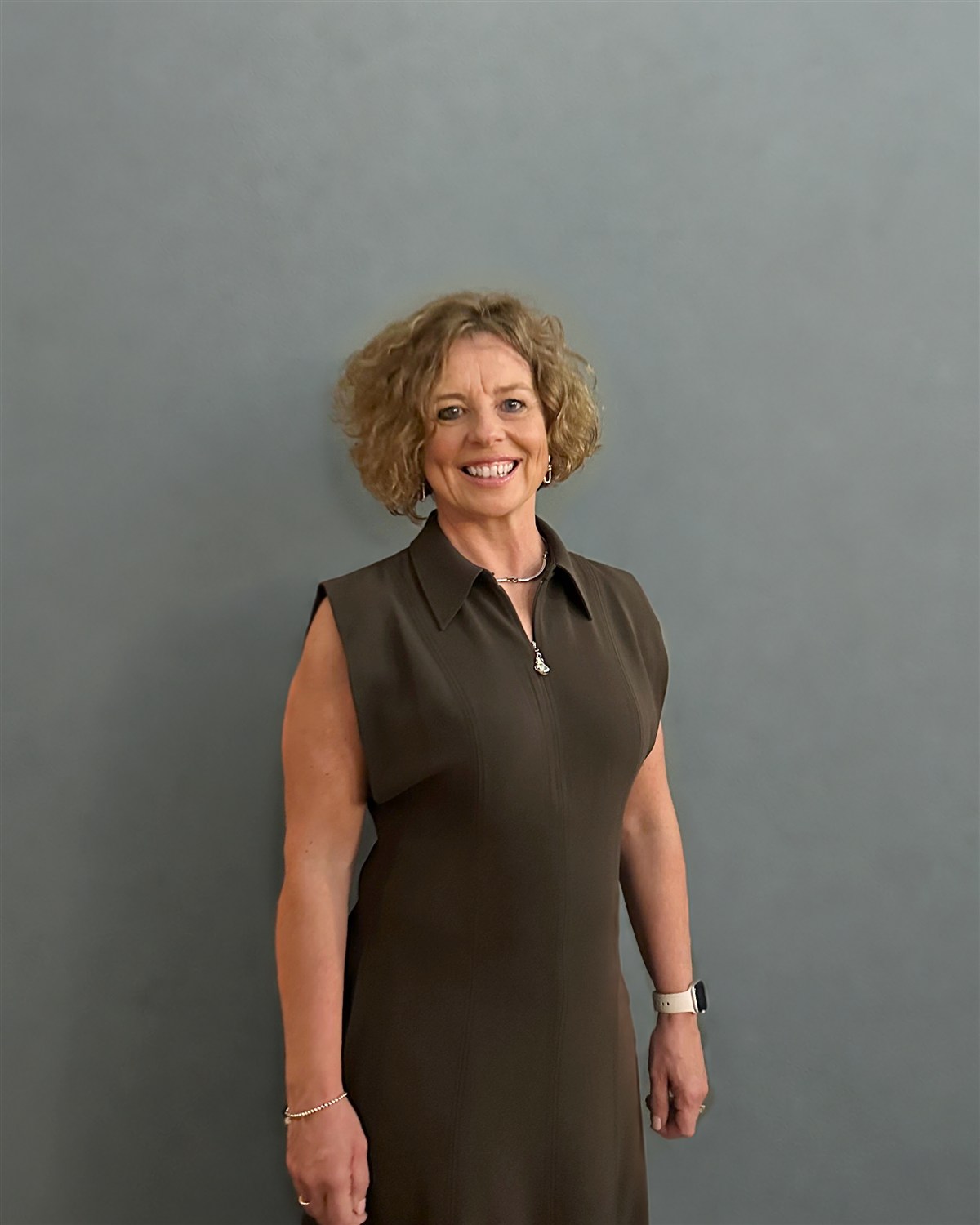 Susan Gibson-Smith smiling in an olive dress against a grey-green wall