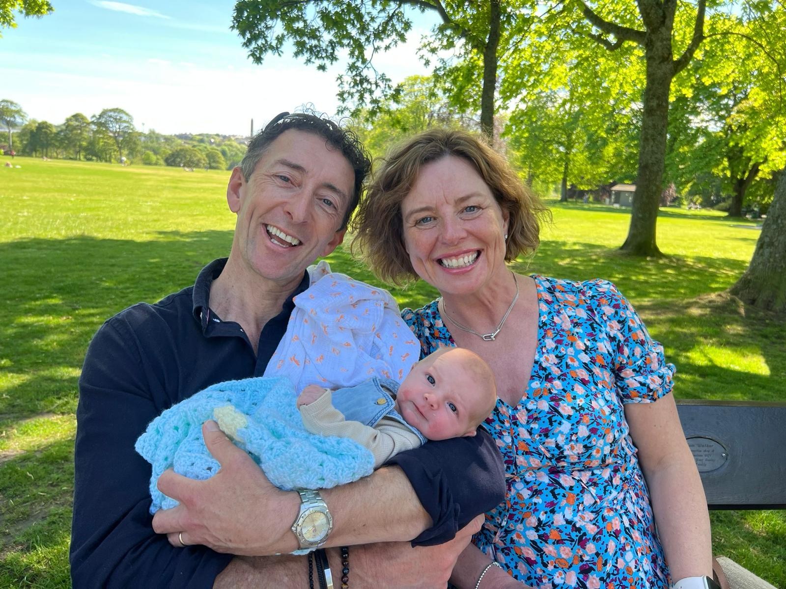 Susan Gibson-Smith on a park bench beside a man holding a baby